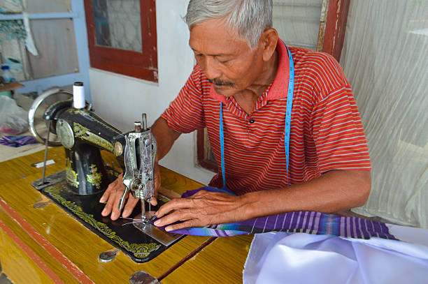 istock Elderly Man Concentrated on Sewing Striped Blue Fabric 2250646025