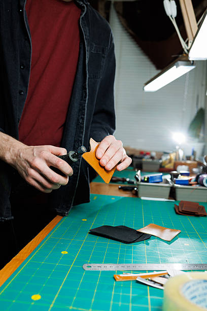 A man's hand holds pieces of leather for a leather wallet in his workshop. The process of working with natural brown leather. The craftsman holds the craft