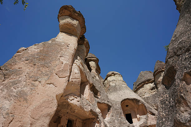 Iconic fairy chimney rock formation with ancient cave dwellings at Goreme Open-Air Museum, Cappadocia, Turkey, under a bright blue sky
