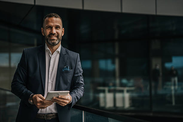 istock Confident businessman holding tablet standing outside office building 2250653816