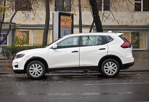 Yerevan Armenia 12.7.2025. A white car is parked on a wet street. The car is parked in front of a building with a sign on it
