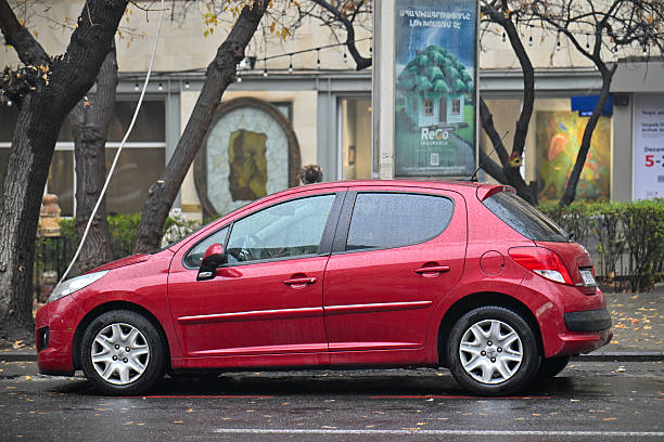 Yerevan Armenia 12.7.2025. A red car is parked on a wet street. The car is parked in front of a building with a large sign on it