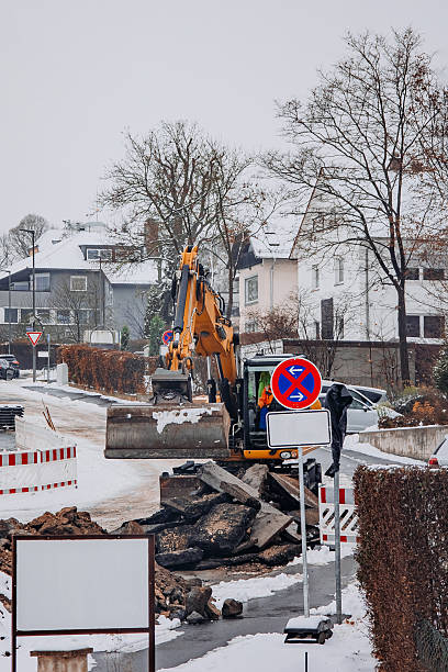 istock Excavator Breaking Asphalt on Winter Road Construction Site 2250656518