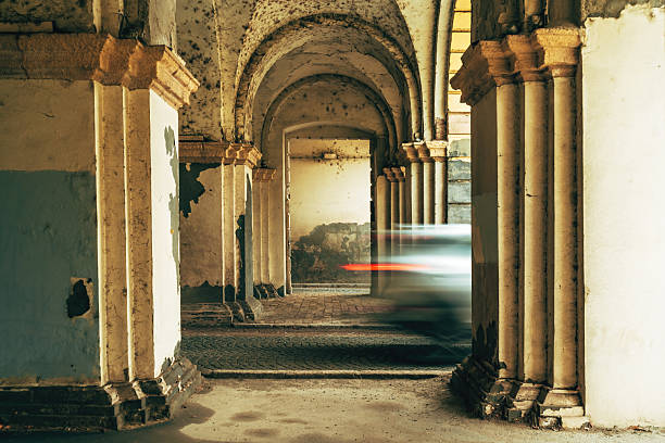 Blurred cars rush through a worn historic corridor, creating a striking contrast between fast urban motion and the aged, crumbling architecture around them. Selective focus.
