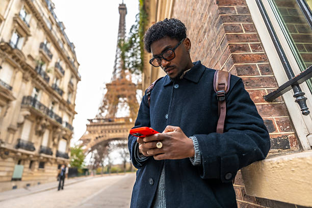 Handsome young man using his smart phone in front of an Eiffel Tower from the street in Paris in France.
