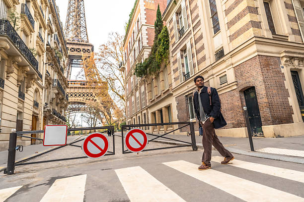Young adult man walking across a crosswalk with the iconic eiffel tower and classic parisian buildings in the background, capturing a travel moment in the city