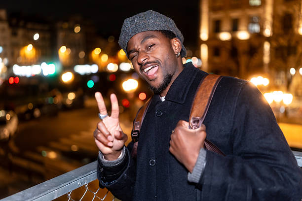 Young man winking and flashing a peace sign in front of paris city lights at night, casual and stylish during an evening out, playful travel portrait with bokeh glow