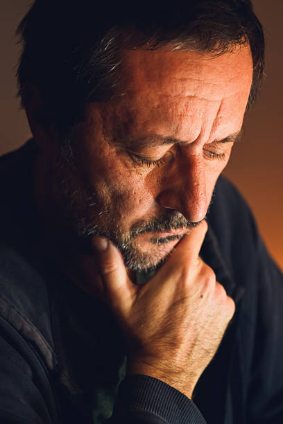 istock Worried man sitting alone in dark room with warm low key light, serious expression and emotional tension. 2250659311