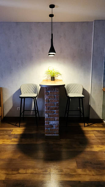 istock Wooden bar table with brick base and two grey cushioned stools stands against grey wall, black pendant lamp above, dark wooden floor, minimal modern kitchen, for interior listing, apartment rental ad. 2250668520