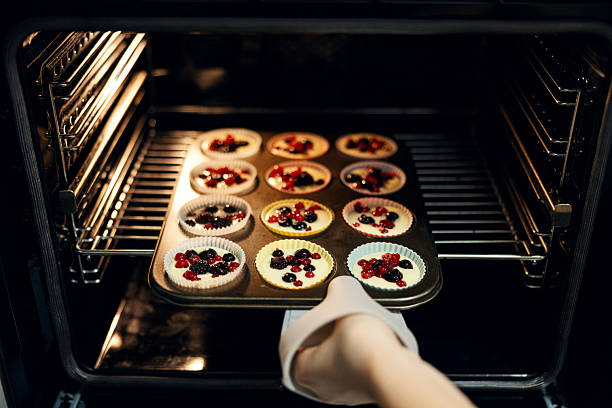 Person placing tray of uncooked berry muffins into a hot oven, preparing homemade fruit-filled pastries in a domestic kitchen