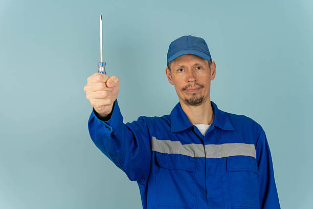 istock Man holds screwdriver in workshop environment during daytime with blue background 2250674388