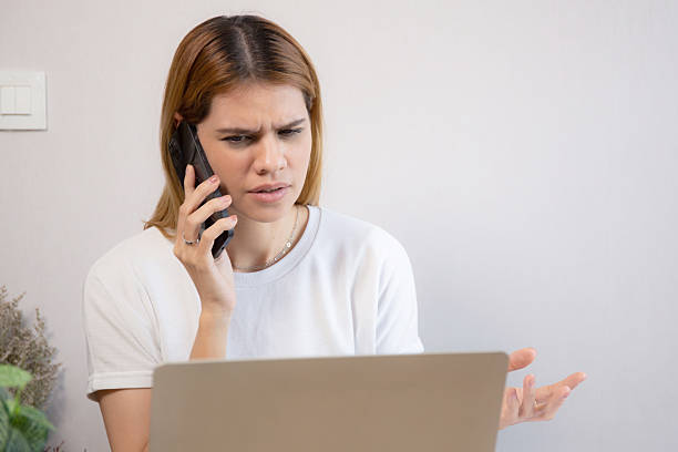 istock Young caucasian businesswoman working on laptop computer while talking on smartphone with stress and upset in office, business woman talking on smart phone with frustrated, business and expression. 2250675711