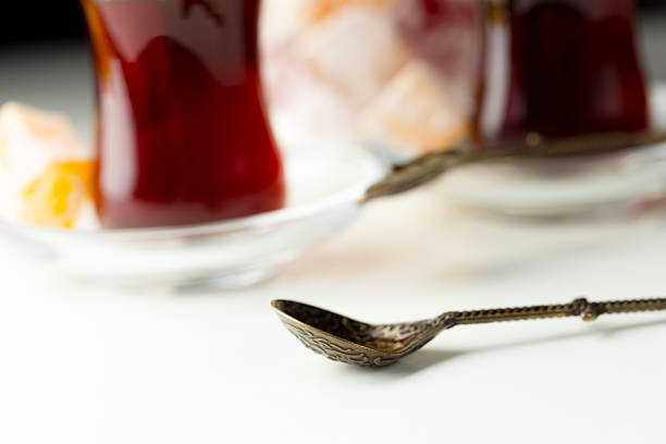 Two glass cups of dark tea sit on a white surface near a vintage spoon, inviting warmth.