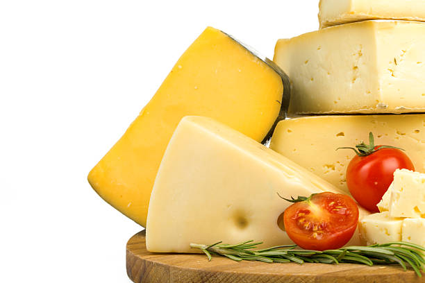 A selection of different cheeses is displayed with cherry tomatoes and herbs on a wooden board.