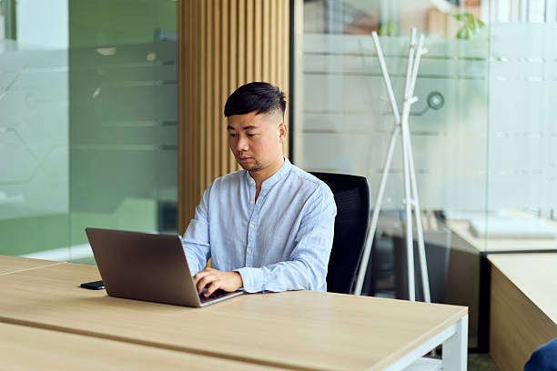 istock Asian Man Working on Laptop at Modern Office Desk in Quiet Collaborative Workspace 2250684182