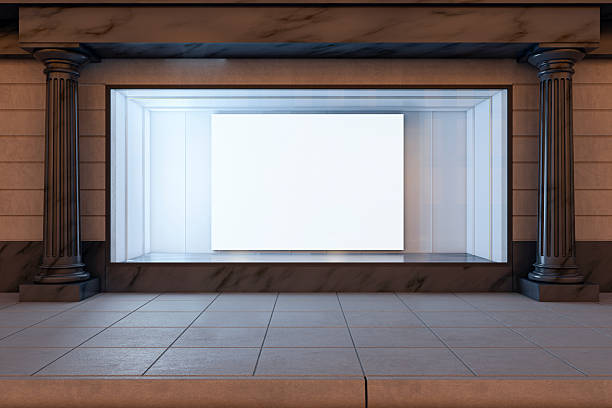 istock Blank storefront window display with clean canvas inside classic retail facade illuminated at night on city street exterior background. 3D Rendering 2250690358