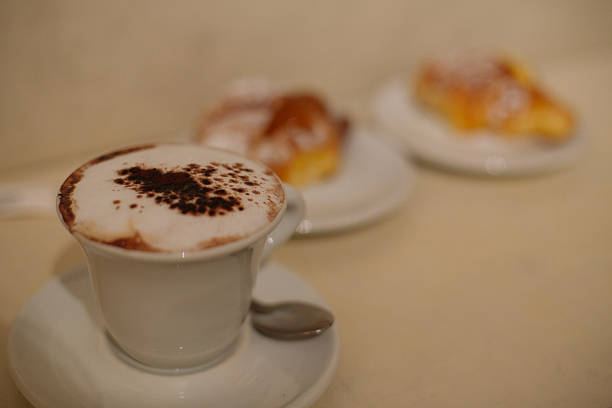 two cups of coffee next to some palm-shaped cookies on yellow tablecloth