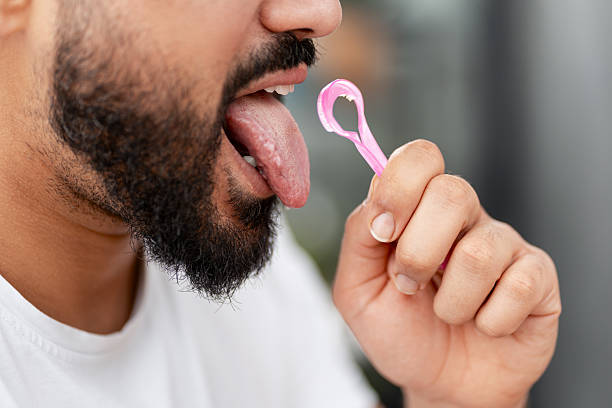 Man cleaning his tongue with a pink scraper, maintaining oral hygiene and fresh breath