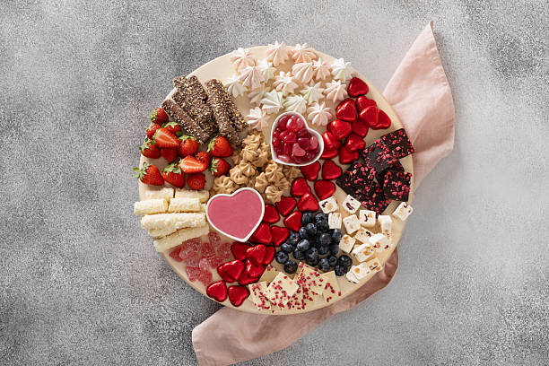 Charcuterie Valentines Day board with chocolate sweets, red hearts, strawberries, blueberries and candies on gray background. View from above.