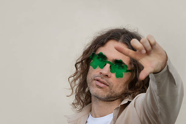 Stylish caucasian adult man 30s wearing green novelty sunglasses. Playful fashion portrait with creative gesture, isolated background, st patricks day concept.