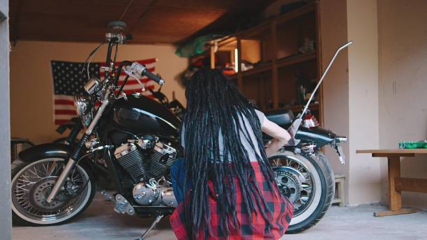istock Biker woman with dreadlocks working on motorcycle in garage with American flag backdrop during daytime, showcasing passion for bike maintenance and repair 2250699854