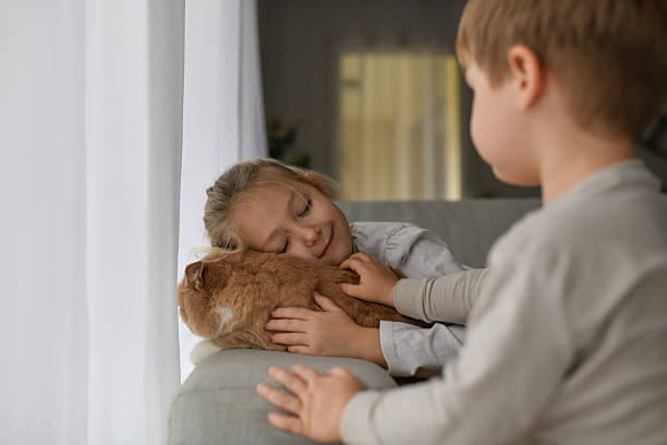 Brother and sister hugging a ginger cat