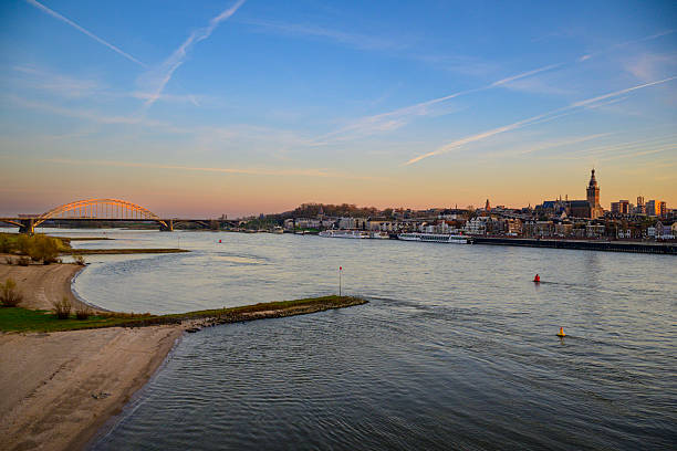 Skyline of the city Nijmegen on the riverbank of the Waal seen from the Waal during sunrise. Various ships are passing the river during this beautiful cold winter sunrise during the start of the day.