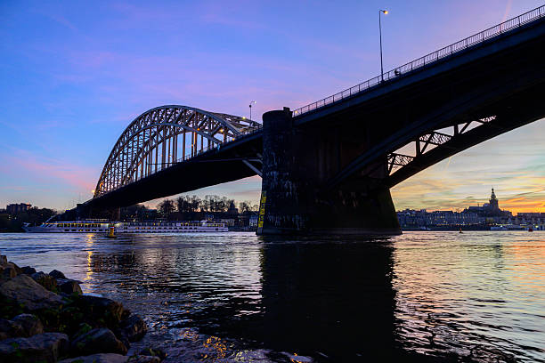 Skyline of the city Nijmegen on the riverbank of the Waal seen from the Waalbrug during sunset. Various ships are passing the river during this beautiful cold winter sunset during the blue hour at the end of the day.