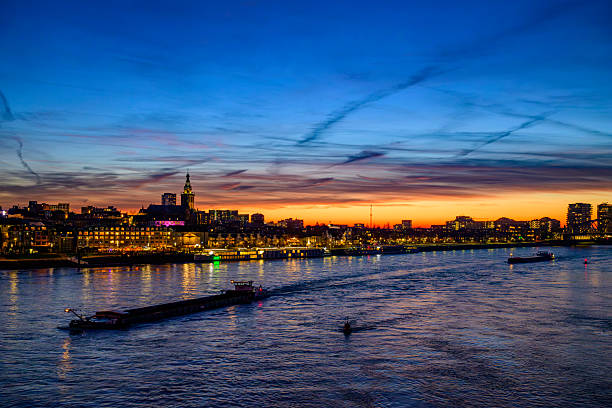 Skyline of the city Nijmegen on the riverbank of the Waal seen from the Waalbrug during sunset. Various ships are passing the river during this beautiful cold winter sunset during the blue hour at the end of the day.