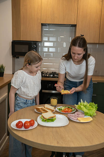 istock Mother and daughter bonding in a modern kitchen, spreading mayonnaise on bread slices while preparing fresh homemade sandwiches together for a healthy family meal. Vertical photo 2250704222