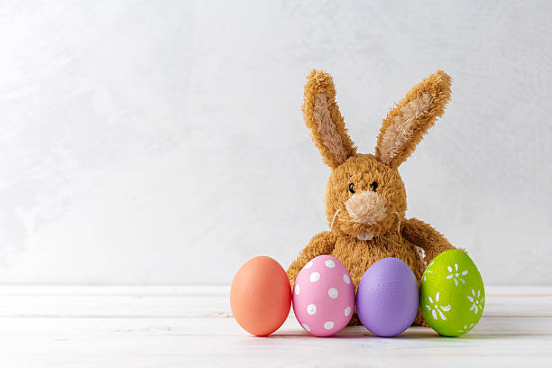 istock Cute bunny toy with colorful Easter eggs on a white wooden surface in springtime 2250705178
