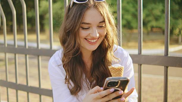 istock Young woman enjoys ice cream while using her smartphone in a park on a sunny afternoon, showing joy and relaxation 2250707830