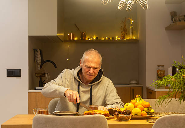 istock A smiling elderly man cuts a piece of pie while sitting at the dining table in the kitchen decorated for Christmas. 2250713781