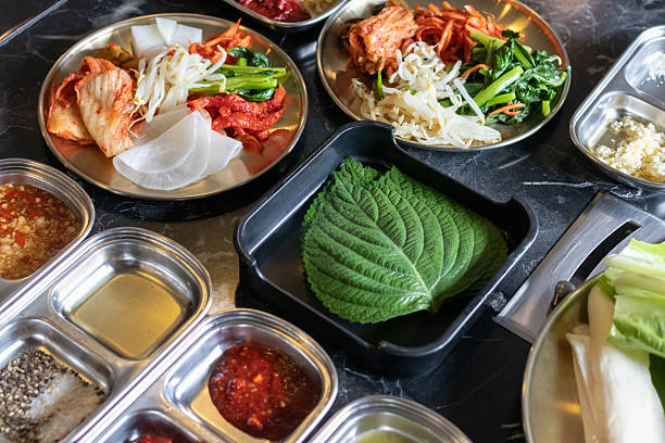 istock Green perilla leaf black tray with assorted Korean banchan including kimchi, pickled radish, bean sprouts and dipping sauces 2250722353