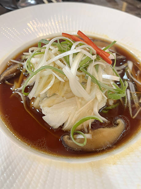 Steamed white fish fillet with shiitake mushroom and scallion in savory brown broth, elegant plated presentation