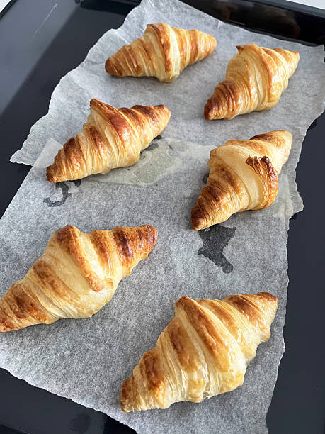 Fresh baked croissant pastry on parchment paper with golden flaky layers, cozy breakfast aroma and warm texture