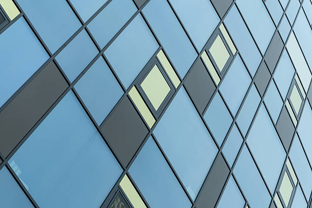 istock Modern building facade with blue and yellow glass windows in geometric grid pattern. Abstract urban architecture with reflective blue panels and asymmetric open windows on a contemporary glass facade. 2250725788