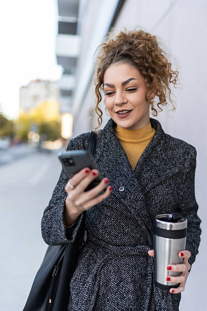 istock Woman checking smartphone and holding coffee travel mug 2250728016