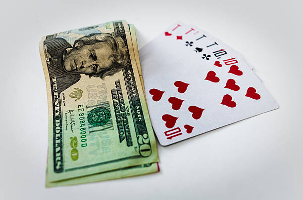 Cash and Playing Cards for Gambling and Poker Game Nights. Twenty-dollar bill placed beside playing cards showing hearts and spades. Gambling concept emphasizes risk and strategies involved in card