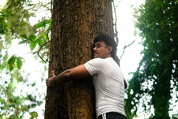 istock Young man hugging tree connecting with nature in forest 2250739574