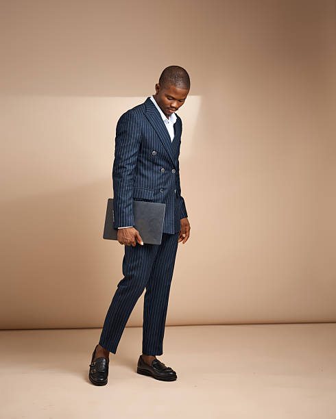 istock Man in pinstripe suit walking while holding a laptop in studio 2250740083