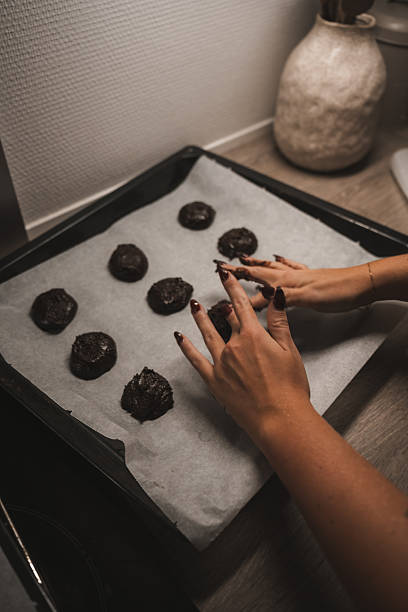 istock Hands shape chocolate cookie dough on a baking tray lined with parchment paper in a warm kitchen. The soft lighting creates a comforting atmosphere, perfect for baking 2250740313