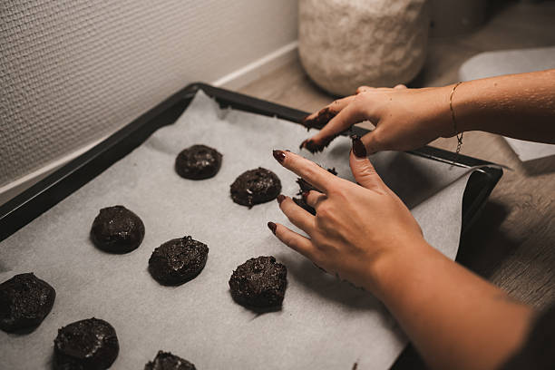 istock Hands shape chocolate cookie dough on a baking tray lined with parchment paper in a warm kitchen. The soft lighting creates a comforting atmosphere, perfect for baking 2250740452