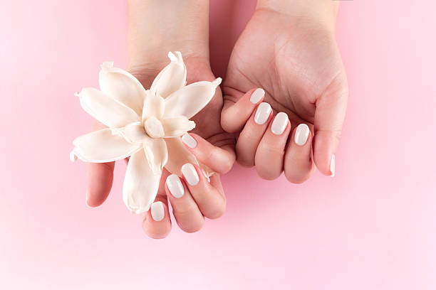 Female hands with beautiful manicure - cloud white dancer nails with white dried flower on pink background