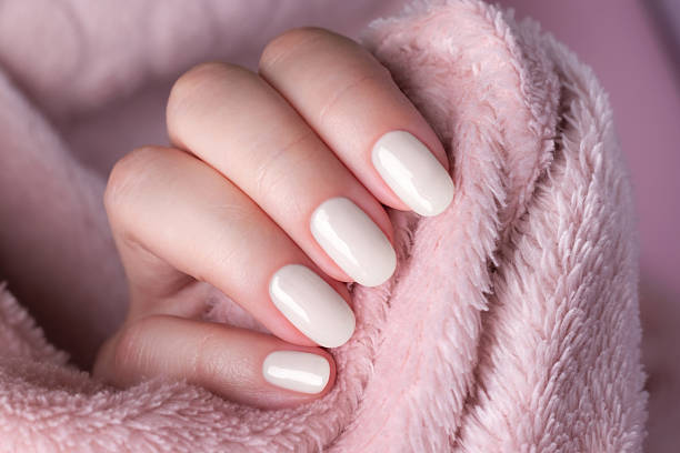 istock Female hand with beautiful manicure - cloud white dancer nails on pale pink fluffy fabric, textile background 2250740564