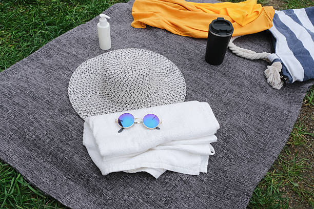beach accessories with beach bag, hat, sunglasses and sunscreen bottle on the blanket over green grass