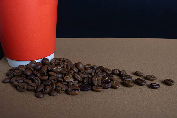 A red paper cup and scattered coffee beans on a brown background
