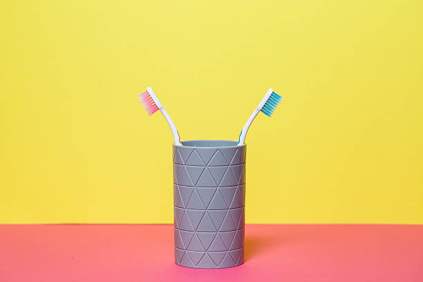 istock Two toothbrushes stand with a gray glass on a yellow background. Toothbrush concept for a couple, living together as the beginning of a family 2250747829