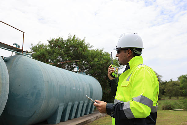istock An industrial worker in a hard hat and fluorescent jacket inspects large water tanks while holding a communication device, Water storage and supply system 2250748070