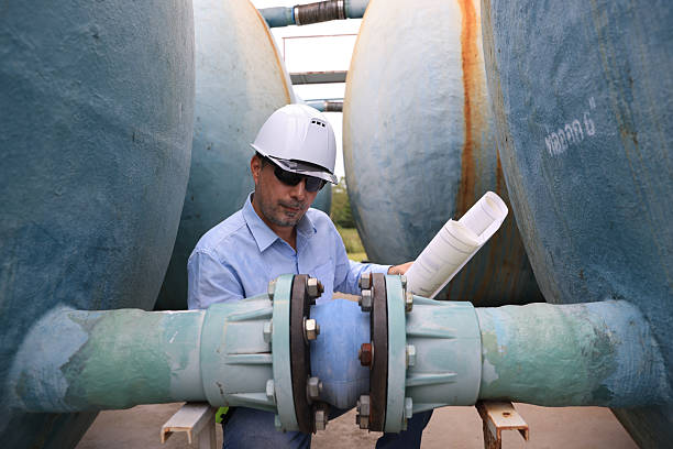 istock A construction professional wearing a hard hat and sunglasses work with walkie-talkie and blueprint drawing at site of large  water tanks and valve. emphasizing communication and teamwork in an industrial environment 2250748092